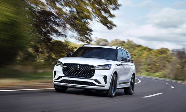 White Lincoln in motion on highway surrounded by trees