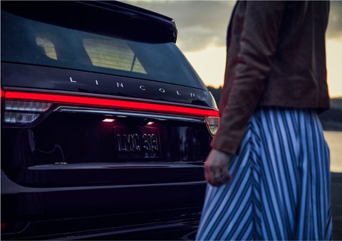 A person is shown near the rear of a 2023 Lincoln Aviator® SUV as the Lincoln Embrace illuminates the rear lights | Lincoln Demo 1 in Wooster OH