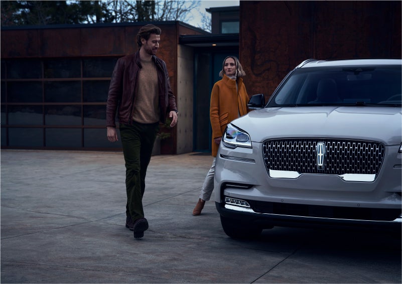 A man and a woman approaching a 2023 Lincoln Aviator® SUV, which illuminates certain lights when they are close | Lincoln Demo 1 in Wooster OH