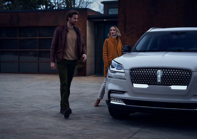 A man and a woman approaching a 2024 Lincoln Aviator® SUV, which illuminates certain lights when they are close | Lincoln Demo 1 in Wooster OH
