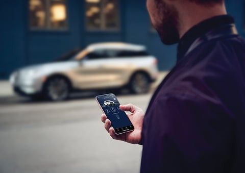 A person is shown interacting with a smartphone to connect to a Lincoln vehicle across the street. | Lincoln Demo 1 in Wooster OH