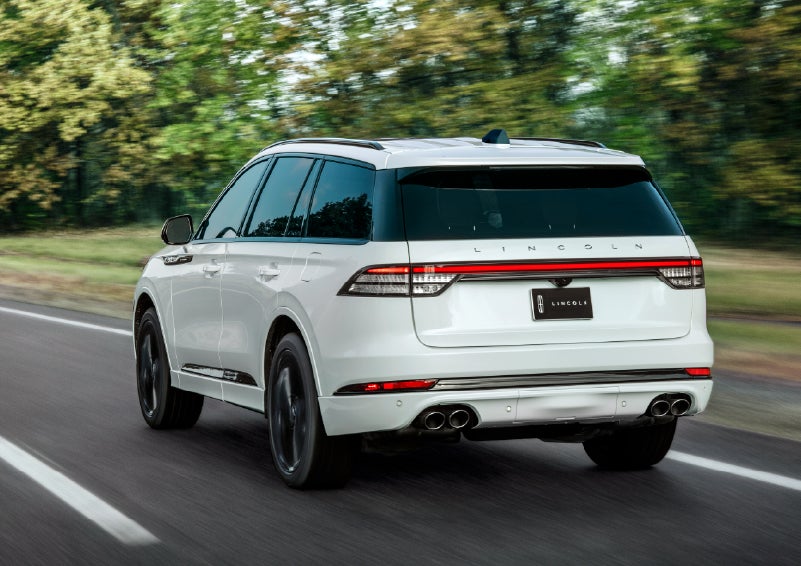 A white 2026 Lincoln Aviator® SUV is being driven away down a road lined with colorful trees. | Lincoln Demo 1 in Wooster OH